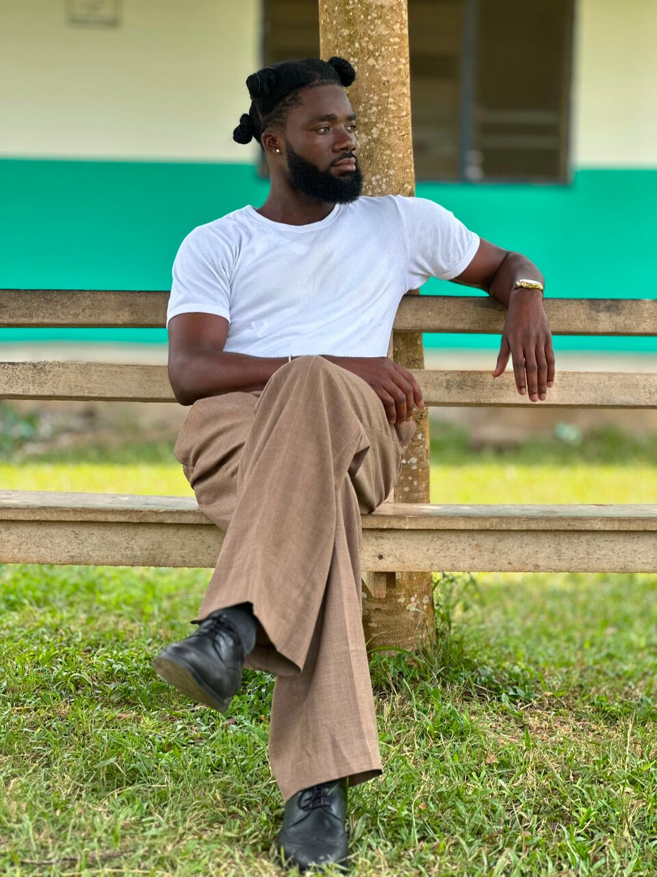 Joseph Panyin, wearing a white T-shirt and his own locs tied up, sitting on a bench outdoors.